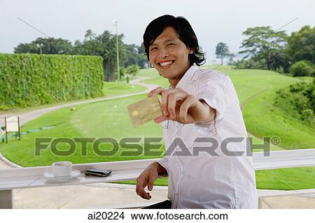 Man holding credit card, smiling at camera, golf course behind him View Large Photo Image Picture - Man holding credit card, smiling at camera, golf course behind him. Fotosearch