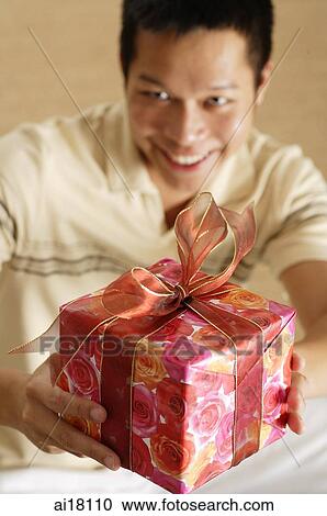 Man holding gift towards camera, smiling View Large Photo Image Stock Image - Man holding gift towards camera, smiling. Fotosearch