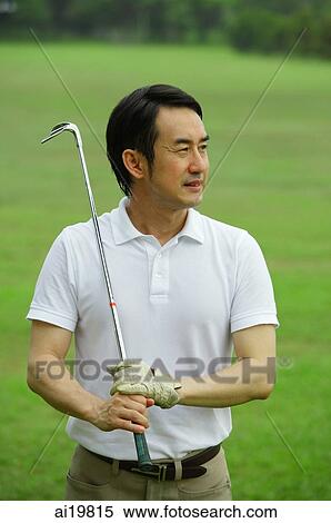 Stock Photography - Man holding golf club, looking away. Fotosearch