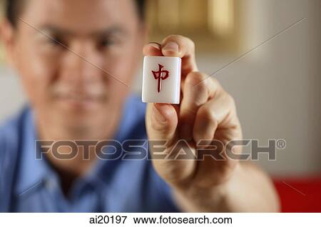Stock Photo - Man holding mahjong dice with Chinese script for Middle on it. Fotosearch