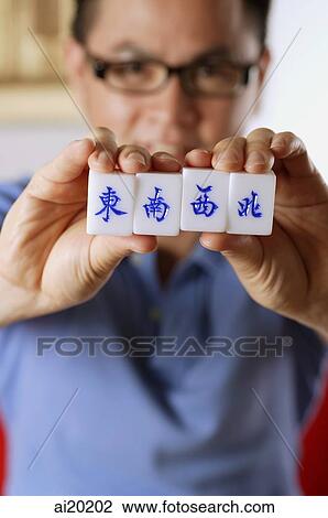Stock Image - Man holding mahjong tiles with Chinese characters for East, South, West and North. Fotosearch