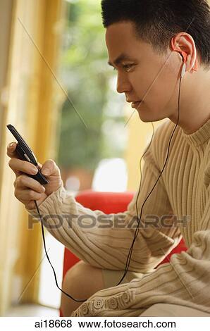 Man holding mobile phone, using earphones View Large Photo Image Stock Photo - Man holding mobile phone, using earphones. Fotosearch