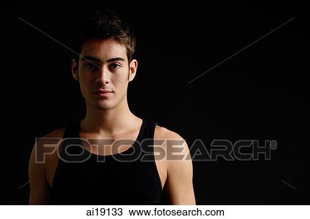 Stock Image - Man in black sleeveless top, standing against black background. Fotosearch