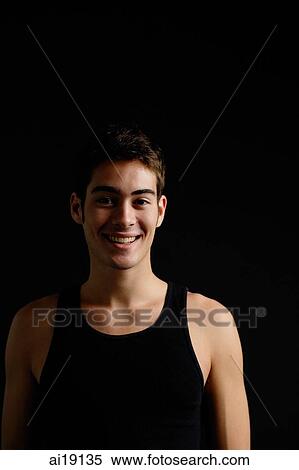 Stock Photography - Man in black sleeveless top, standing against black background, looking at camera, smiling. Fotosearch