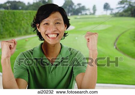 Stock Image - Man in green polo shirt, smiling at camera, hands raised as fists. Fotosearch