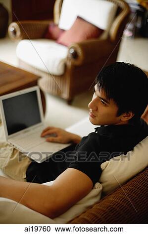 Stock Image - Man in living room with laptop on lap. Fotosearch
