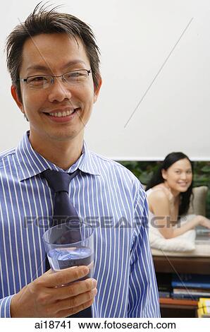 Man in striped shirt and tie, holding glass of water, woman in the background View Large Photo Image Stock Image - Man in striped shirt and tie, holding glass of water, woman in the background. Fotosearch