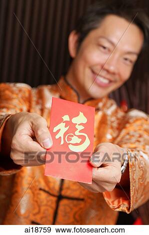 Stock Photo - Man in traditional Chinese clothing holding red packet. Fotosearch