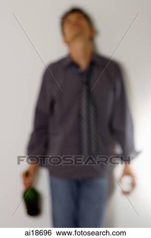 Stock Photograph - Man leaning against wall holding bottle and glass. Fotosearch
