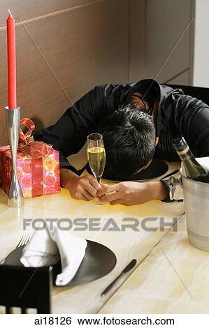 Stock Photograph - Man leaning head down on table, holding champagne glass. Fotosearch