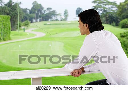 Stock Photo - Man leaning on railing, looking out at golf course. Fotosearch