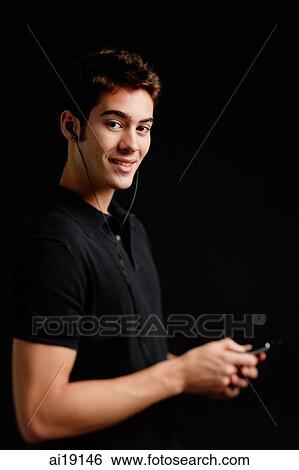 Man listening to MP3 player, looking at camera View Large Photo Image Stock Photograph - Man listening to MP3 player, looking at camera. Fotosearch