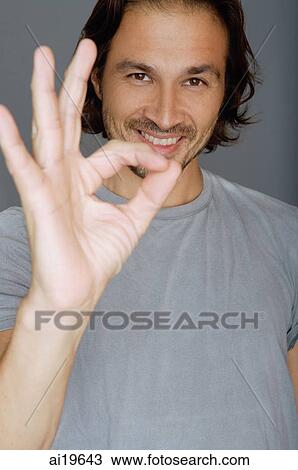 Stock Image - Man looking at camera, making hand sign. Fotosearch