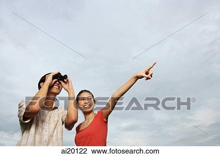 Stock Image - Man looking through binoculars, woman next to him pointing in the distance. Fotosearch