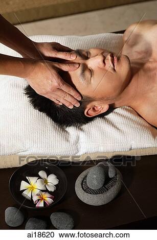 Stock Image - Man lying down, having head massaged. Fotosearch