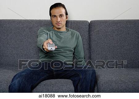 Stock Photo - Man on sofa holding TV remote control. Fotosearch