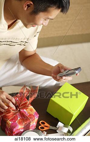 Man opening present and looking at mobile phone View Large Photo Image Stock Photo - Man opening present and looking at mobile phone. Fotosearch