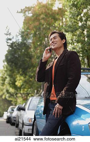 Picture - Man outdoors, leaning on car, using mobile phone. Fotosearch