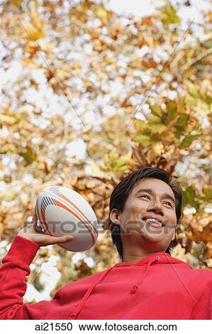 Stock Image - Man outdoors, preparing to throw a rugby ball. Fotosearch