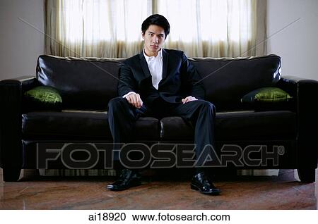 Stock Image - Man seating on sofa, looking at camera. Fotosearch