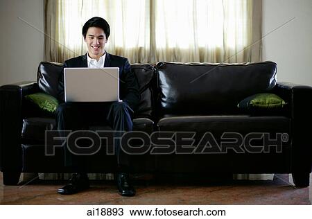Man seating on sofa, using laptop View Large Photo Image Stock Image - Man seating on sofa, using laptop. Fotosearch