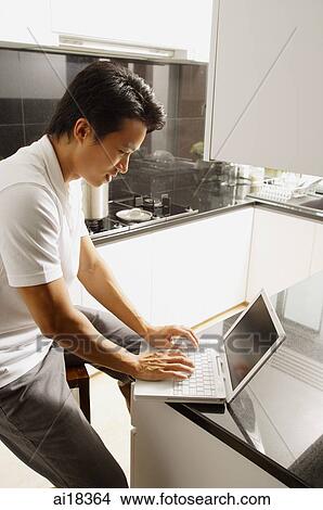 Man sitting at kitchen counter, using laptop View Large Photo Image Picture - Man sitting at kitchen counter, using laptop. Fotosearch