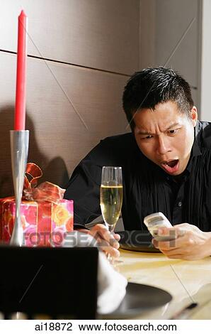 Man sitting at table, looking at mobile phone, mouth open View Large Photo Image Stock Image - Man sitting at table, looking at mobile phone, mouth open. Fotosearch