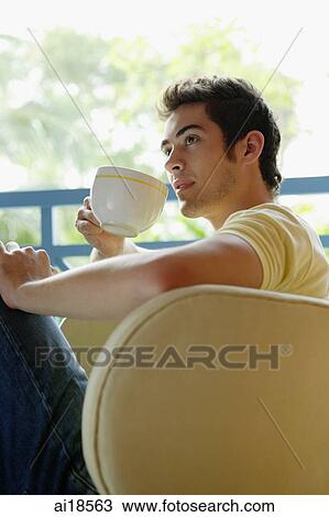 Man sitting on armchair, drinking from cup View Large Photo Image Stock Image - Man sitting on armchair, drinking from cup. Fotosearch