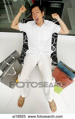 Stock Photography - Man sitting on chair, yawning, shopping bags around him. Fotosearch