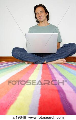 Stock Photo - Man sitting on striped carpet with laptop, looking at camera. Fotosearch