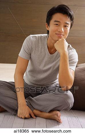 Stock Photography - Man sitting with legs crossed, hand on chin, smiling at camera. Fotosearch
