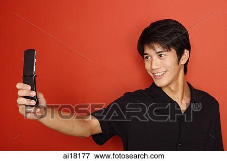 Man standing against red wall, holding mobile phone View Large Photo Image Stock Photo - Man standing against red wall, holding mobile phone. Fotosearch