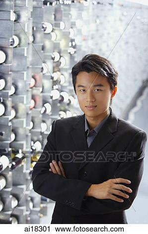Stock Image - Man standing in wine cellar, arms crossed, looking at camera. Fotosearch