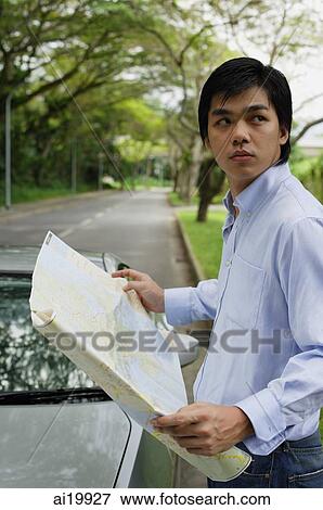 Stock Photo - Man standing next to car, holding map, looking over shoulder. Fotosearch