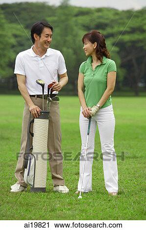 Stock Image - Man standing with golf bag, smiling at woman next to him. Fotosearch