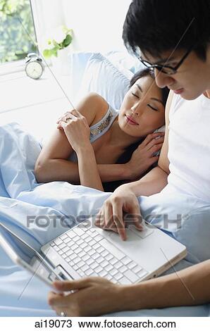 Man using laptop, woman lying next to him, sleeping View Large Photo Image Stock Image - Man using laptop, woman lying next to him, sleeping. Fotosearch