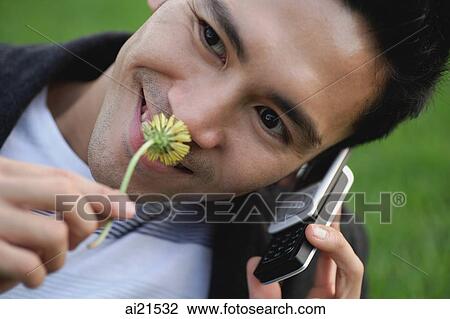 Stock Image - Man using mobile phone, smelling flower. Fotosearch