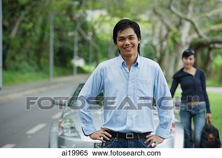 Man with hands on hips, standing in front of car, woman in the background with luggage View Large Photo Image Stock Photography - Man with hands on hips, standing in front of car, woman in the background with luggage. Fotosearch