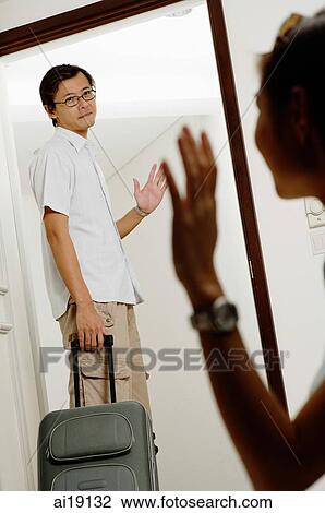 Man with luggage, standing at door, waving to woman in foreground View Large Photo Image Stock Image - Man with luggage, standing at door, waving to woman in foreground. Fotosearch