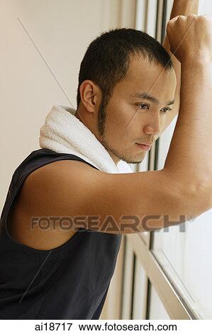 Stock Photo - Man with towel around his neck, leaning on window. Fotosearch