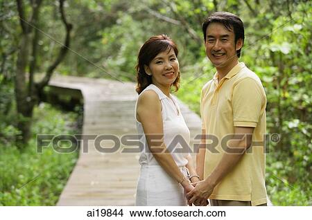 Picture - Mature couple holding hands, looking at camera. Fotosearch