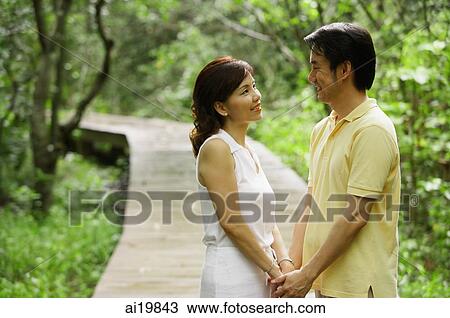 Stock Image - Mature couple holding hands, looking at each other. Fotosearch