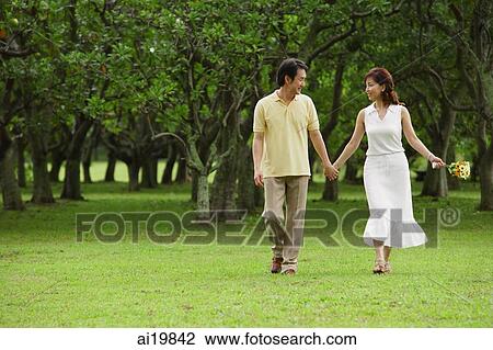 Stock Image - Mature couple in park, holding hands, walking. Fotosearch