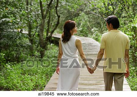 Stock Photography - Mature couple walking in park, holding hands, rear view. Fotosearch