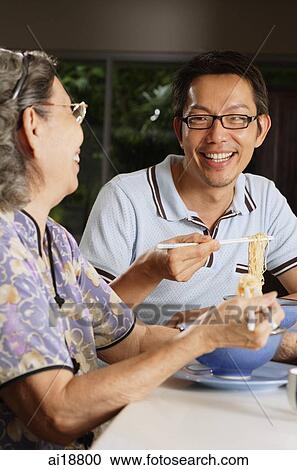 Stock Image - Mature son and mother having noodles. Fotosearch