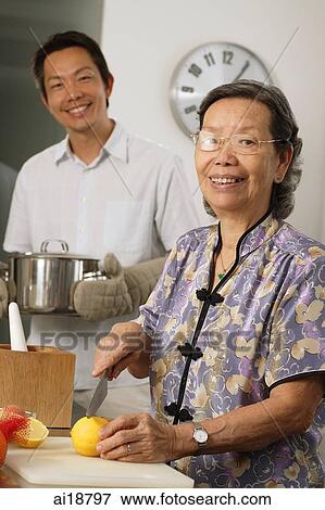 Stock Photo - Mature son and mother in the kitchen, woman chopping lemons, man holding pot. Fotosearch