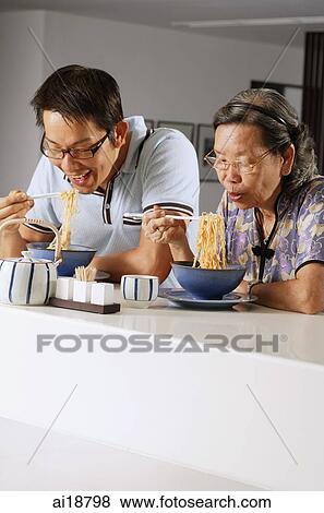 Mature son and mother sitting at kitchen counter eating noodles View Large Photo Image Stock Photo - Mature son and mother sitting at kitchen counter eating noodles. Fotosearch