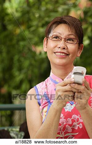 Stock Photo - Mature woman holding mobile phone, looking away. Fotosearch