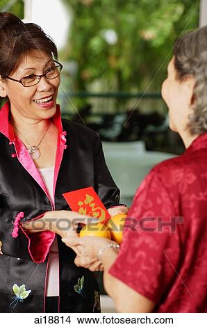 Mature woman presenting senior woman with oranges and red packet View Large Photo Image Picture - Mature woman presenting senior woman with oranges and red packet. Fotosearch