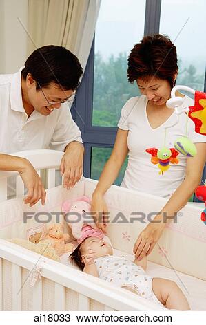 Stock Image - Mother and father looking at baby in crib. Fotosearch